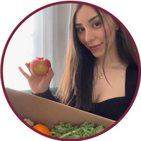 Woman holding an apple next to a box of fresh vegetables